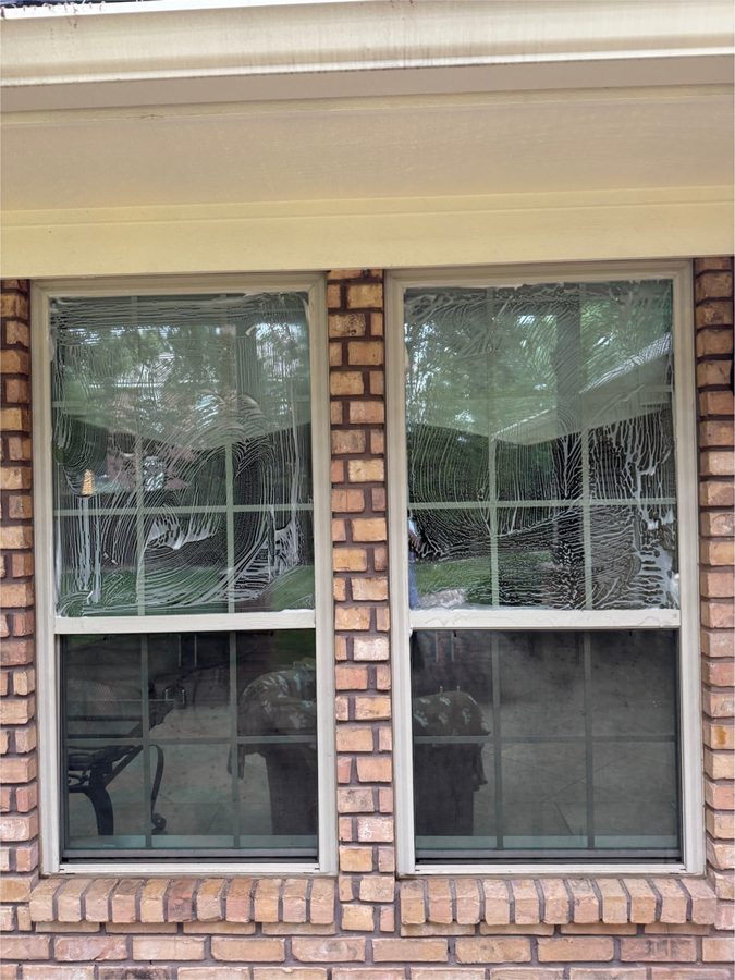 Windows covered in cleaning foam mid-wash on a brick home